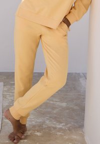 Gelbe Baumwoll-Sweatpants mit entspannter Passform, gerippten Bündchen, seitlichen Taschen und sichtbaren Nähdetails, kombiniert mit einem passenden Oberteil.