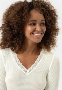 Witte geribde top met een V-hals en kantafwerking. Beschikt over een gestructureerde stof en een aansluitende silhouet. Geen patronen of extra versieringen.