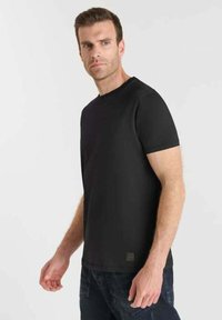 T-shirt nera a maniche corte in un morbido misto cotone, con scollatura a girocollo classica e un piccolo etichetta del marchio sull'orlo.
