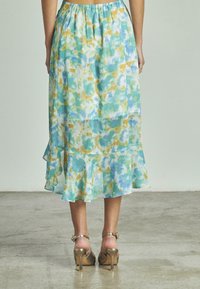 Gonna maxi leggera e fluida in toni di blu, verde e arancione con motivi tie-dye, caratterizzata da un orlo arricciato. Abbinata a sandali con tacco dorati.