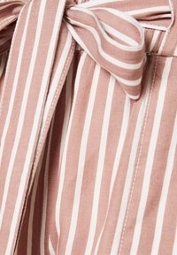 Bezramienna odzież w miękkim, jasnoróżowym materiale z pionowymi białymi paskami, z wiązanym kokardą w talii dla dodatkowego akcentu.