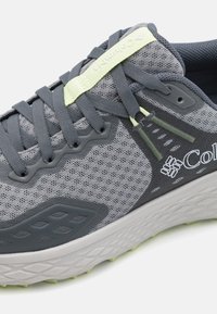 Harmaa verkkomainen juoksukenkä, jossa on tekstuuri, mustia yksityiskohtia, vaaleanvihreä nauhasuojus ja pehmustettu pohja, jossa on kuvioitu kulutuspinta.