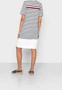 Sukienka t-shirt w paski z krótkimi rękawami; biała baza, czarne paski, czerwona akcentująca pasek i prosta sylwetka. Nosić z granatowymi sandałami.