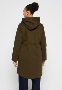 Olijfgroene middellange jas met een capuchon, trekkoord in de taille en lange mouwen. Zachte textuur zonder zichtbare patronen of hardware.