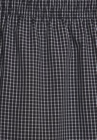 Juodas audinys su mažais baltais tinklelio raštais, su gumbeliais, sudarančiais vertikalius raukšles.