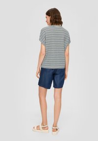 Gestreepte top in marineblauw en wit met korte mouwen, gecombineerd met donkere denimshorts en lichte, gestructureerde sandalen.