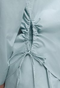 Γαλάζιο ύφασμα με λεπτομέρεια ελαστικής ρίγας και δεμένη φιόγκο στο πίσω μέρος, που αναδεικνύει την υφή του υφάσματος και τις ραφές.