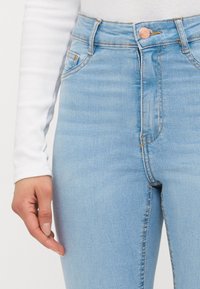 Ljusblå högmidjade jeans i denim med en knappslutning framtill, fem fickor och subtila blekningar. Strukturerad tyg med sömdetaljer.