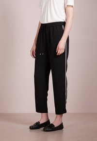 Svarta korta byxor med dragsko i midjan, med vita sidosträck. Slät tyg med avslappnad passform och avsmalnande ben. Matchas med svarta loafers.