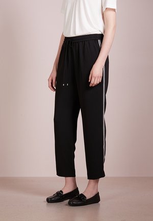 Pantalones cortos negros con cintura elástica, que incluyen franjas laterales blancas. Tejido suave con un corte relajado y piernas ajustadas. Combinados con mocasines negros.