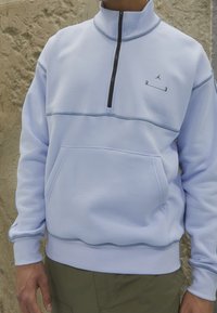Světle modrý mikina s čtvrtinovým zipem, přední kapsou, kontrastními šedými švy a malým logem na hrudi. Měkká látka, volný střih.