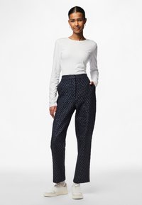 Pantaloni blu navy in tessuto con vita alta e gamba larga, caratterizzati da un sottile motivo a rombi e tasche laterali, abbinati a una maglietta bianca a maniche lunghe.