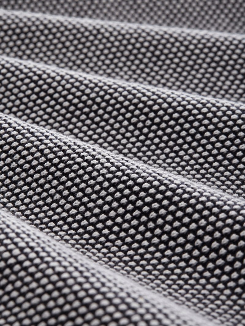 Zbliżenie na czarno-białą tkaninę o fakturze z małymi wypukłymi kropkami i falistymi zagnieceniami, tworzącymi wzorzystą powierzchnię.