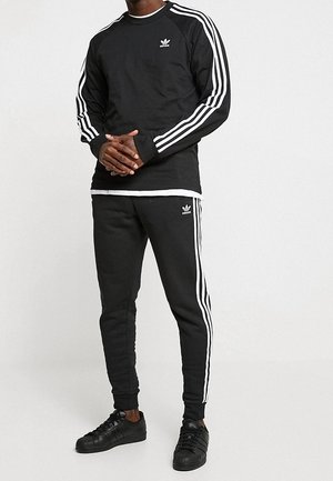 Zwarte sportieve sweatshirt met witte strepen op de mouwen, gecombineerd met bijpassende zwarte joggingbroek met zijstrepen, en zwarte sneakers.