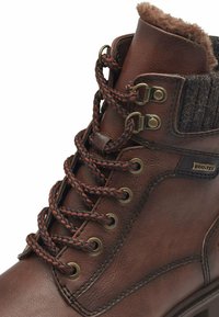 Bruine leren enkellaars met een textielkraag, gevlochten veters en metalen oogjes; heeft een DUO-TEX-label aan de zijkant.