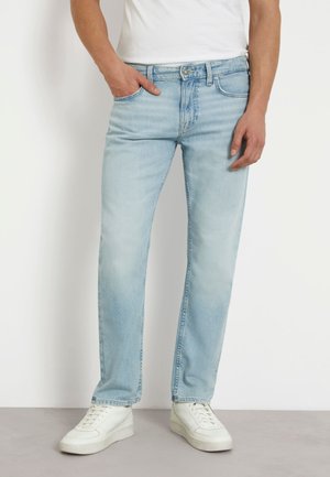 Jeans in denim blu chiaro con taglio dritto, caratterizzati da dettagli di cucitura e design a cinque tasche. Abbinati a sneaker bianche.
