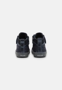 Botines de ante azul marino con patrón de estrellas, tira de Velcro y suelas de goma. Logo de GEox en la parte trasera, lengüeta texturizada para facilitar el calzado.