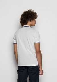 Camisa polo branca com detalhes em azul marinho no colarinho e nas mangas, mangas curtas e bainha reta, usada com calças escuras.