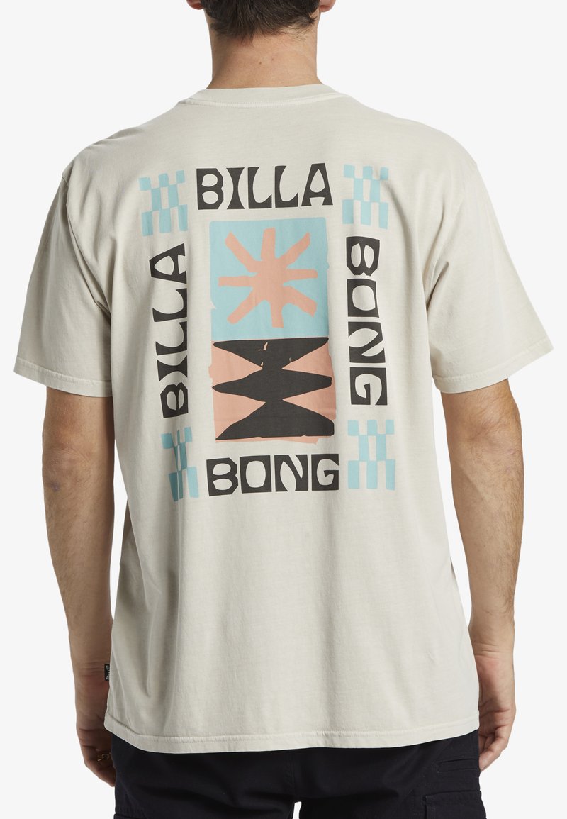 Camiseta de algodón de color beis claro con un diseño gráfico audaz en la parte posterior, que presenta patrones y texto alternando en negro, rosa y azul.