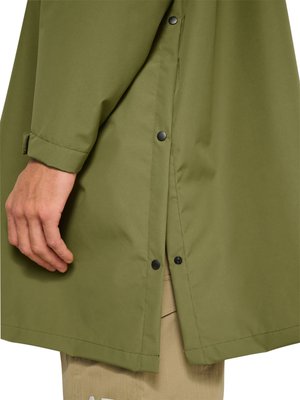 Ręka obok oliwkowo-zielonego płaszcza sięgającego do bioder, z widocznymi czarnymi zatrzaskami i pod spodem beżowe spodnie.