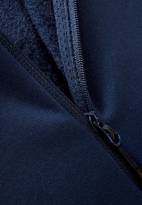 Tessuto navy con zip, dalla consistenza liscia; dettaglio zip visibile e fodera interna in pile; bordi con cuciture per la durata.