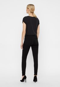 Top preto de manga curta combinado com jeans skinny pretos. O conjunto apresenta um design simples, textura suave e uma silhueta elegante.