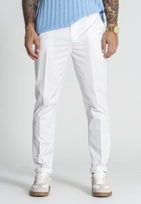 Weiße Baumwollhosen mit schlanker Passform, die eine glatte Textur und umgeschlagene Säume aufweisen. Kombiniert mit hellen Sneakers.
