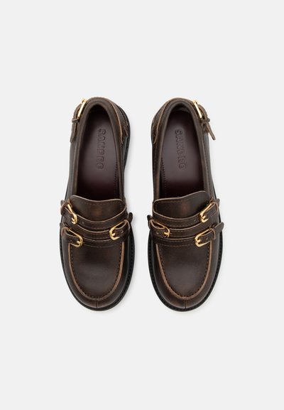 Zapatos de cuero marrón con doble hebilla dorada, con una punta redondeada y costuras de contraste, montados sobre una suela de goma negra.