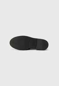 Black shoe sole with a smooth texture, featuring a subtle logo imprint and a rounded shape. The design includes horizontal grooves for grip.