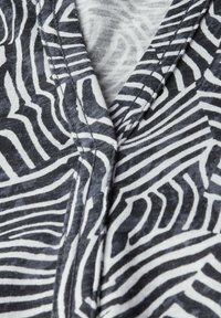 Tissu rayé noir et blanc avec un motif ondulé, présentant un design en V et une texture douce, mettant en avant des coutures cousues et des accents lisses.