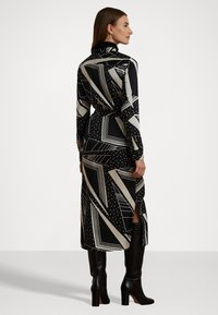 Långärmad klänning i svart och krämvit med geometriska mönster, med knäppning bak och sidoklipp, tillverkad av lättviktig tyg.