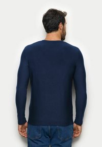 Granatowa koszula z długim rękawem, wykonana z gładkiego materiału, z okrągłym dekoltem. Tył jest gładki, bez wzorów czy widocznych akcentów.