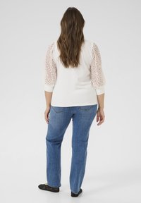 Blusa blanca con mangas abullonadas de encaje, combinada con vaqueros azul de corte recto y bailarinas negras. Tejido suave y patrón intrincado en las mangas.