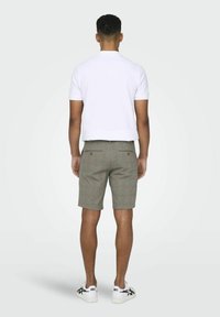 Polo shirt blanc pour homme, à manches courtes, associé à un short à carreaux gris, coupe slim, avec deux poches arrière. Porté avec des baskets blanches.