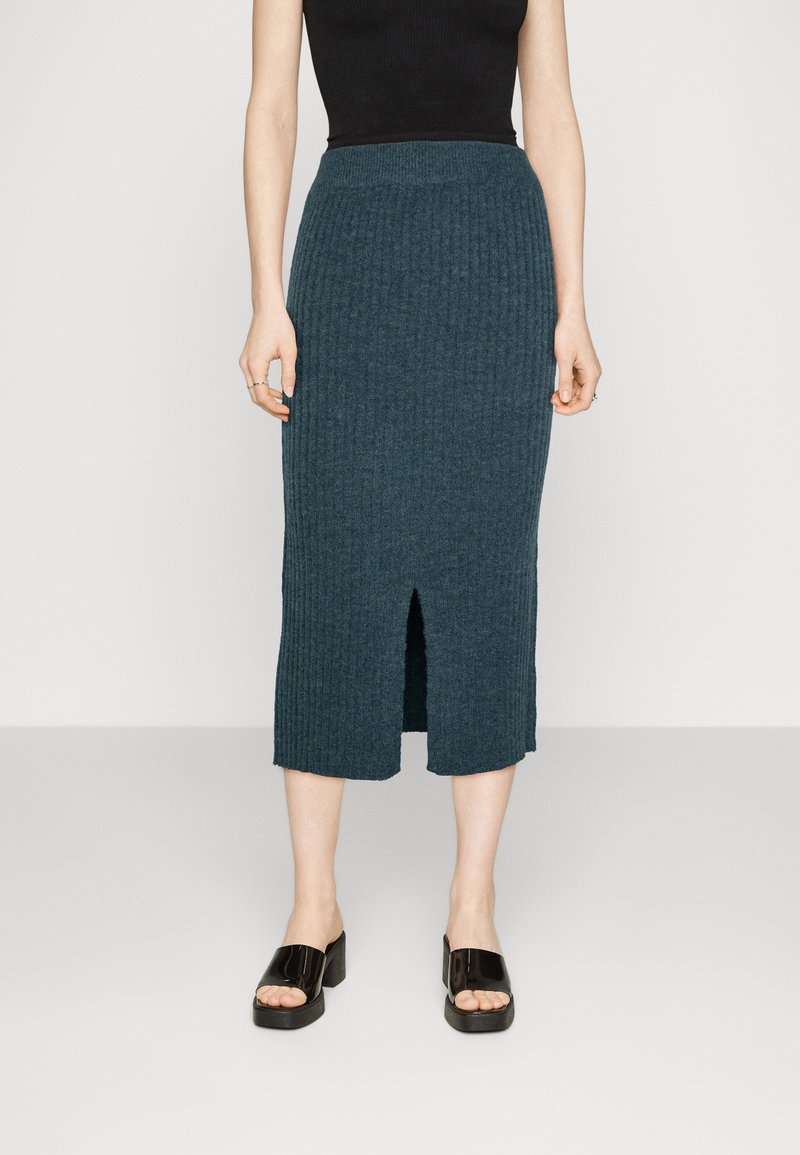 Jupe midi en tricot teal avec une texture côtelée, une fente sur le côté et une taille cintrée, assortie à des sandales à talons carrés ouvertes noires.