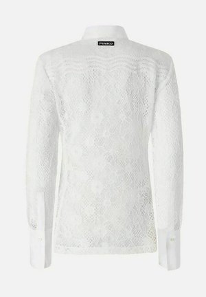 Blouse blanche à manches longues en dentelle avec des motifs floraux, des poignets boutonnés et une petite étiquette noire "PINKO" au col arrière.