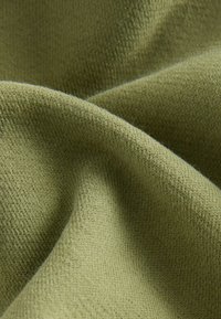 Tejido de punto verde oliva con una superficie suave y texturizada y patrones de costura visibles, que muestra pliegues suaves y ondulaciones.
