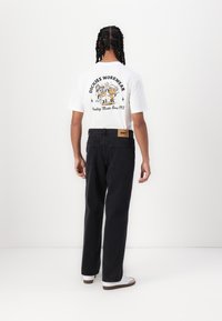 White T-shirt featuring a graphic print on the back, paired with black high-waisted jeans, and white sneakers with brown accents.