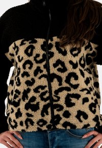 Giacca in fleece nera e marrone con motivo leopardato sulla parte inferiore, chiusura con zip e texture morbida.