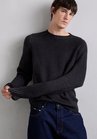 Charcoal gray knitted sweater with a crew neck, ribbed cuffs, and hem, paired with blue denim jeans. Textured fabric and relaxed fit.