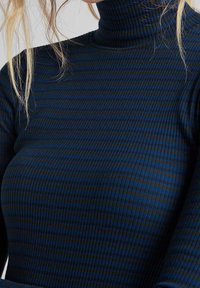 Haut à col roulé côtelé en bleu foncé avec fines rayures noires. Présente une coupe ajustée et des manches longues dans un tissu doux et texturé.