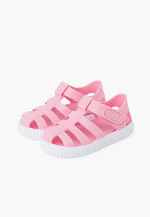 Sandales en caoutchouc rose avec un design de strap, dotées d'une semelle blanche et d'un motif croisillons. Accentuées par un logo sur le côté.