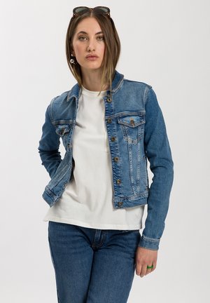 Denim jacket in light blue, featuring a button-up front, two chest pockets, and long sleeves, paired with a plain white shirt.