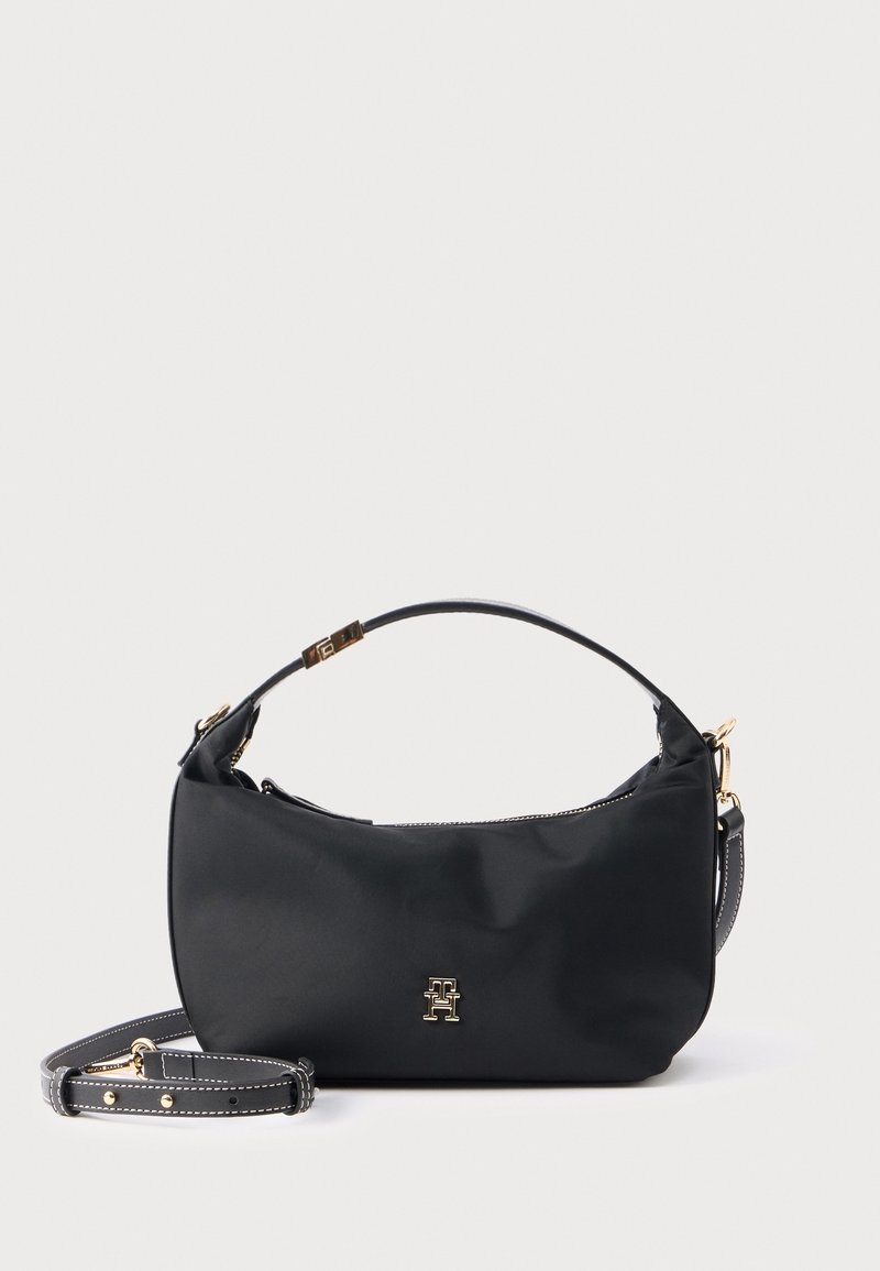Petit sac à main noir avec poignée sur le dessus, bandoulière amovible, quincaillerie dorée et logo métallique à l'avant sur fond uni.