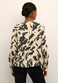 Blusa de manga larga en tejido crema con un estampado animal abstracto en negro. Con un corte relajado y puños abotonados. Se muestra la vista trasera.
