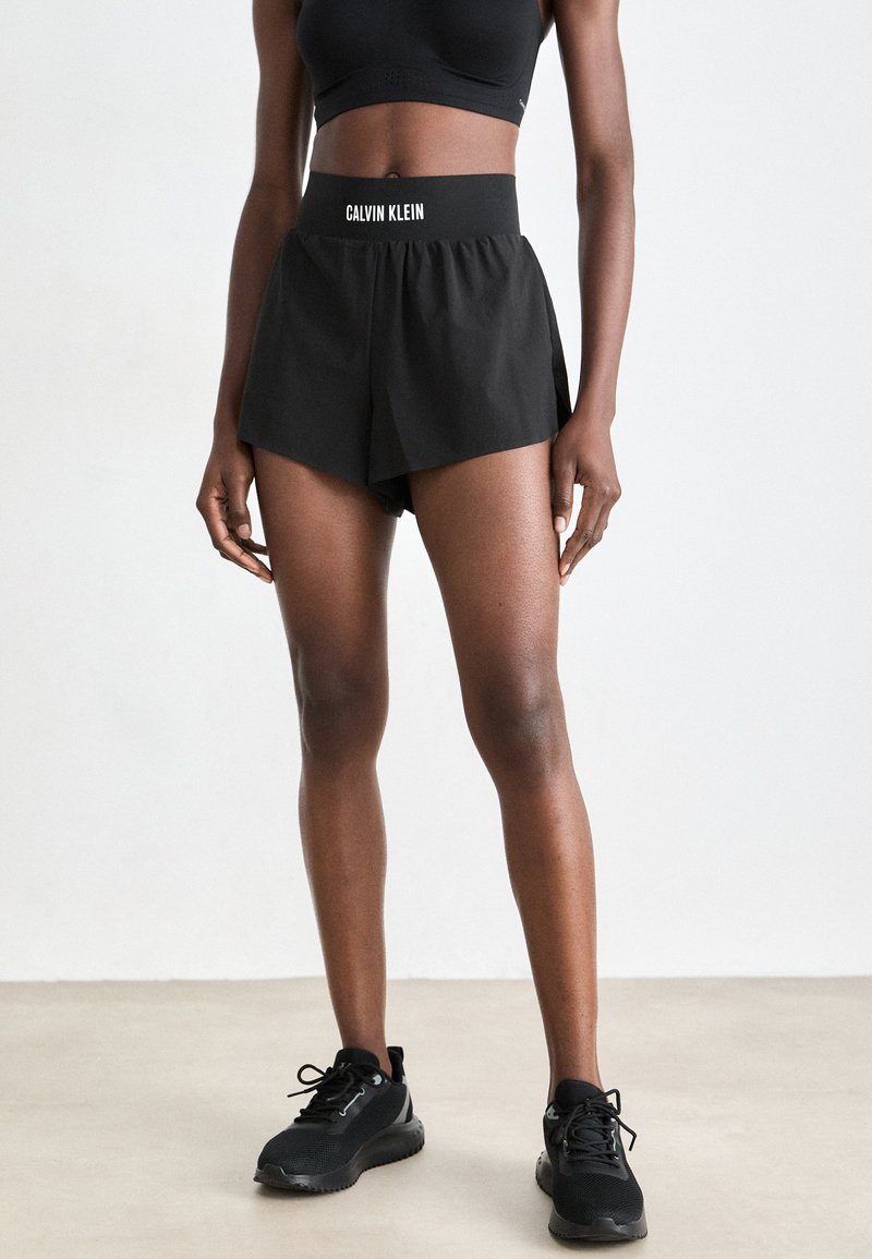 Shorts sportivi neri con una cintura larga che presenta il logo "CALVIN KLEIN". Il tessuto è morbido; il design include una vestibilità ampia con pantaloni interni.