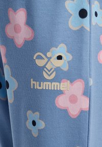 Lichtblauwe stof met een bloemenpatroon met roze en blauwe bloemen, en een gouden logo met de tekst "hummel" onderaan.