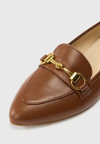 Mocassin en cuir marron à bout pointu, orné d'une chaîne dorée et de détails de surpiqûres. Texture lisse avec un design élégant.
