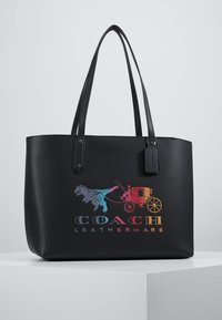 Sort læder-tote taske med dobbelt håndtag, der har et flerfarvet Coach-logo med et vogn- og dinosaurdesign på forsiden.