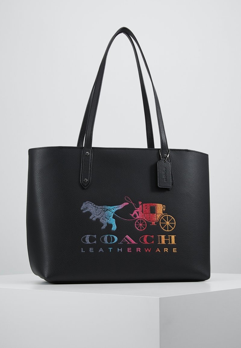 Sort læder-tote taske med dobbelt håndtag, der har et flerfarvet Coach-logo med et vogn- og dinosaurdesign på forsiden.